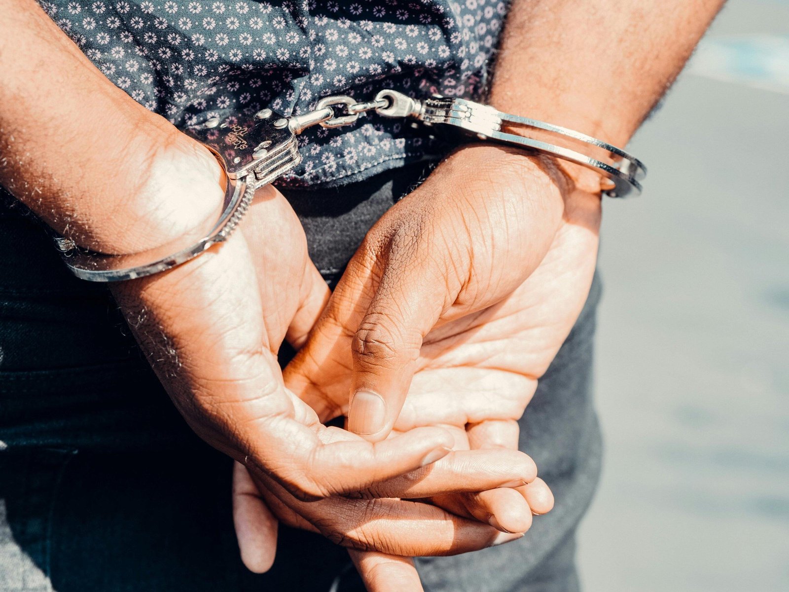 Close-up of hands cuffed with silver handcuffs. NSW Goods in Custody offence.