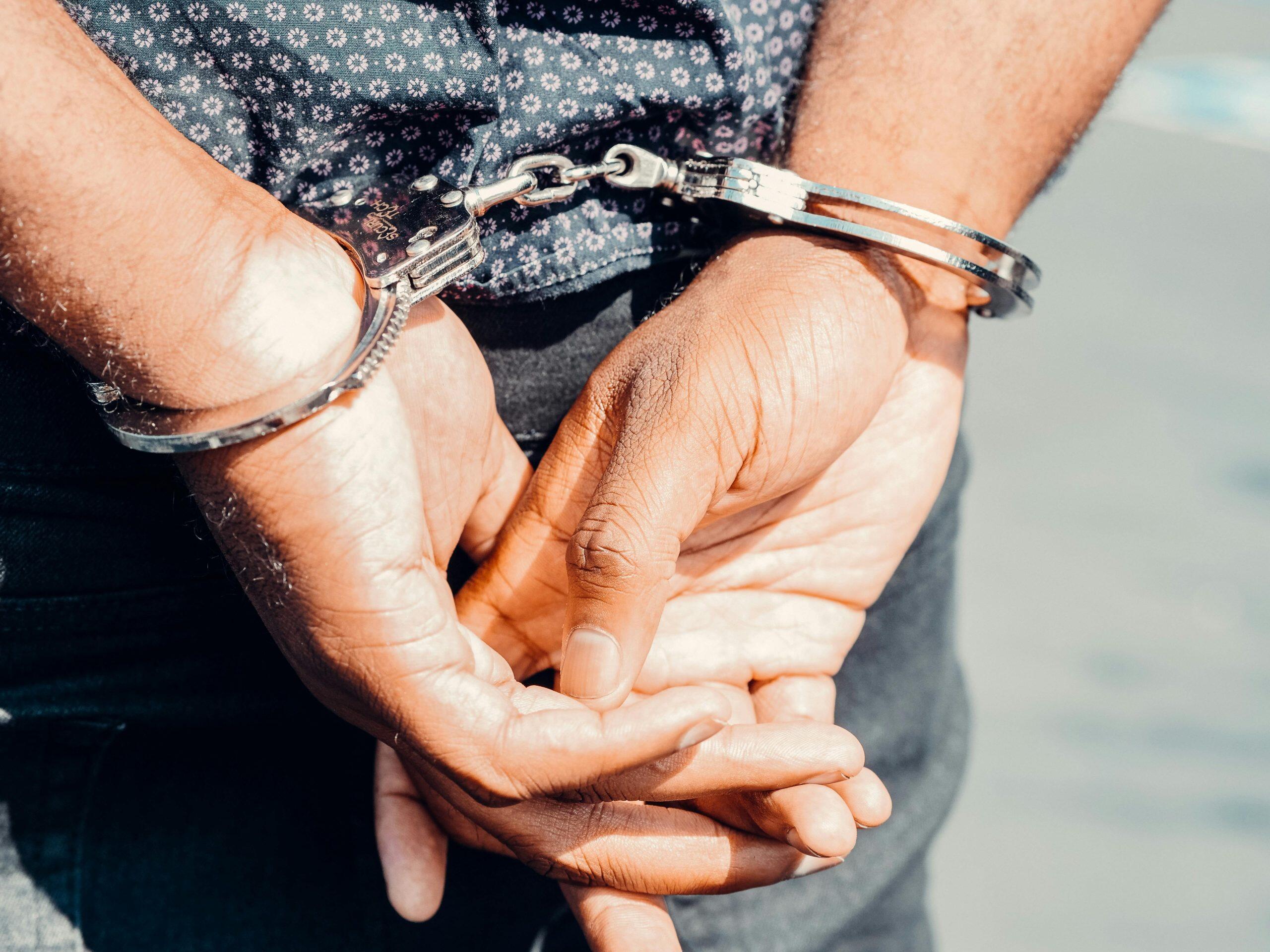 Close-up of hands cuffed with silver handcuffs. NSW Goods in Custody offence.