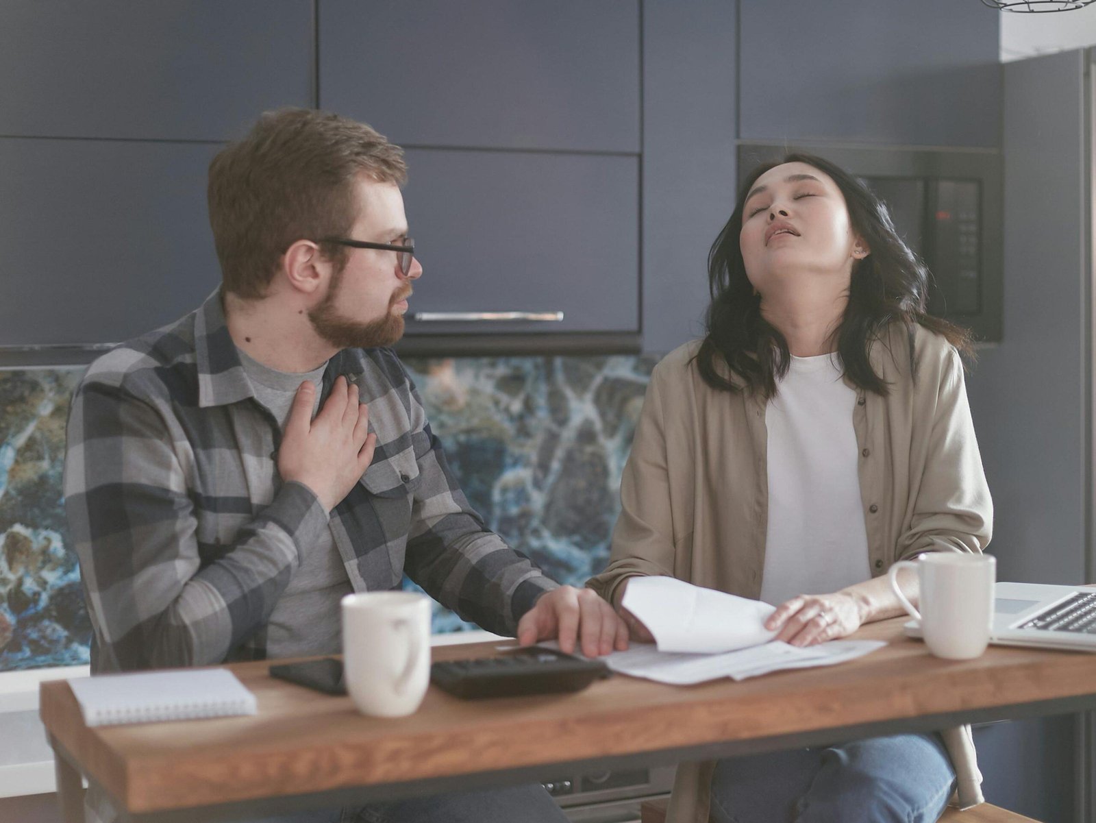 Stressed couple reviewing paperwork at kitchen table, discussing finances or legal documents.