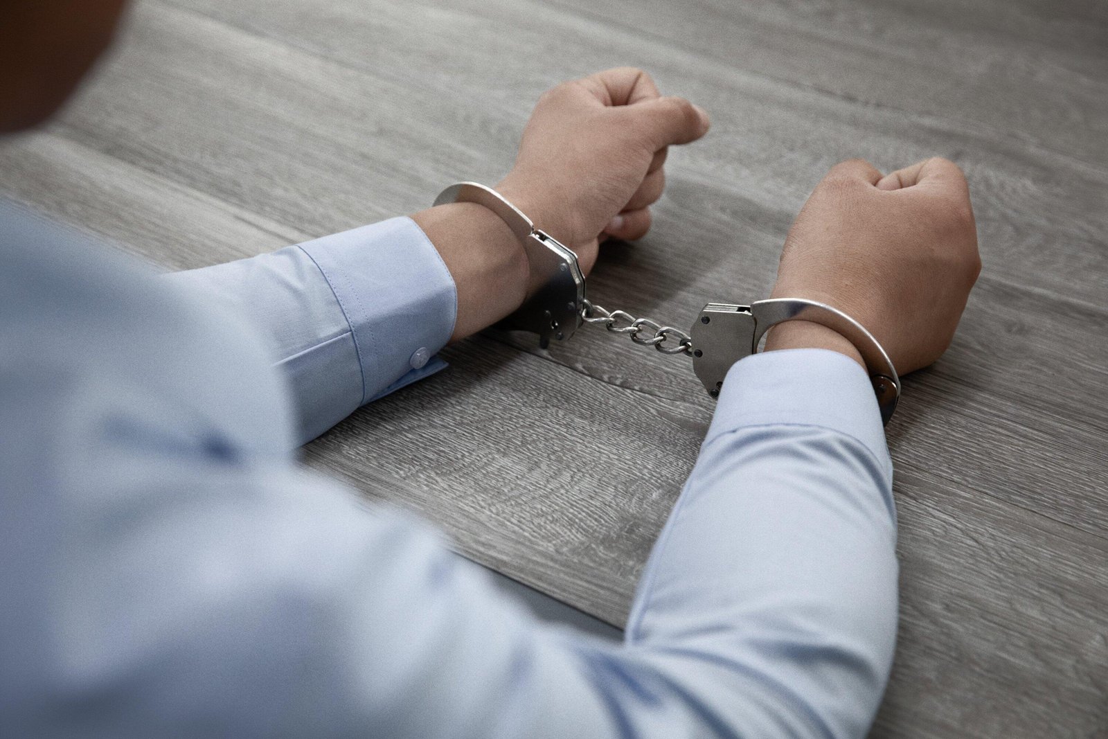 Person in handcuffs on a wooden table, related to legal penalties