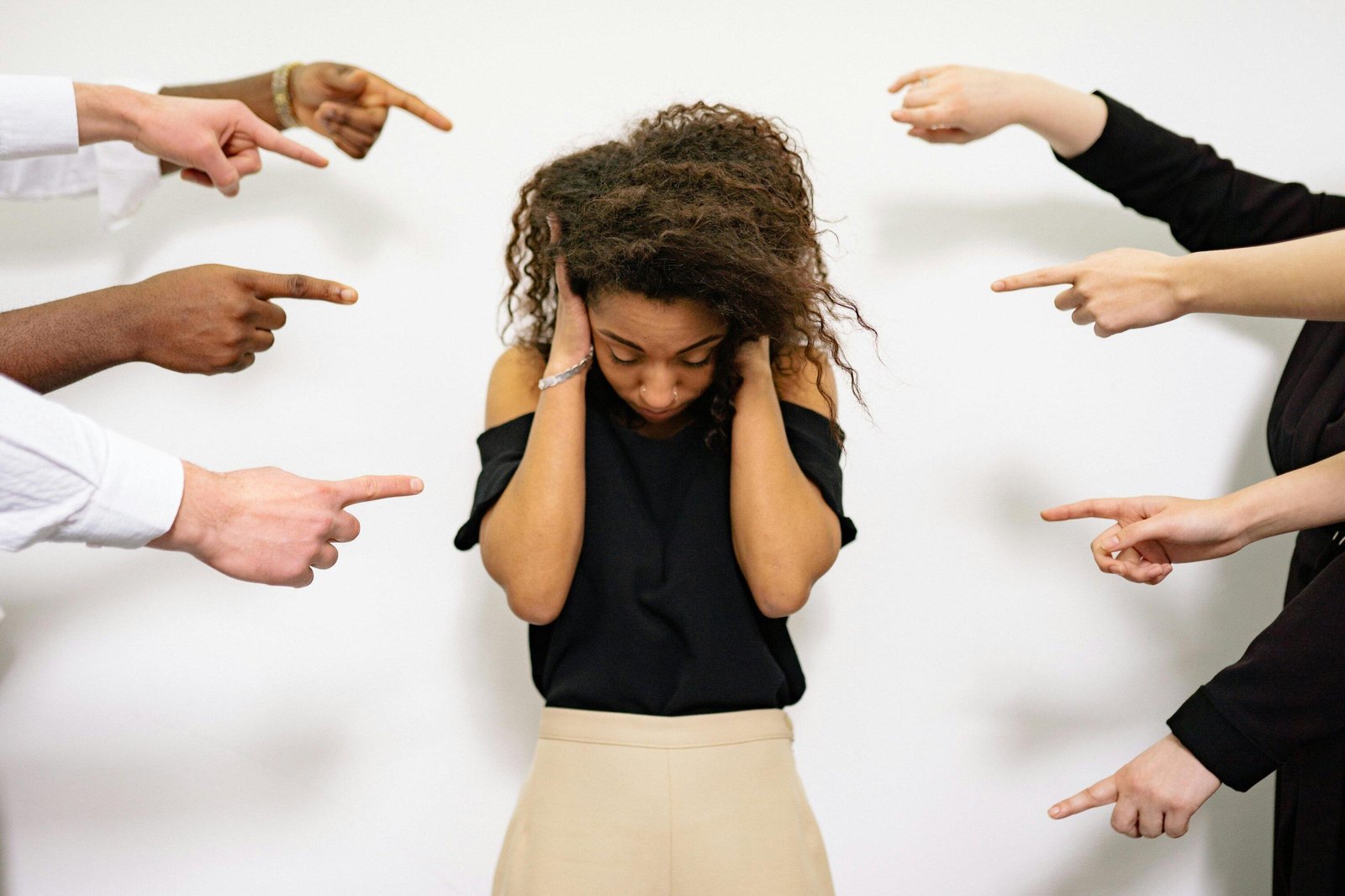 Upset woman surrounded by pointing fingers, illustrating the feeling of being stalked or intimidated.