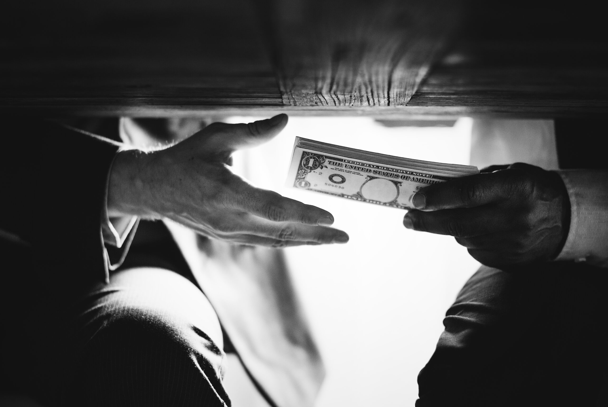 Underside view of a clandestine exchange of money under a table.