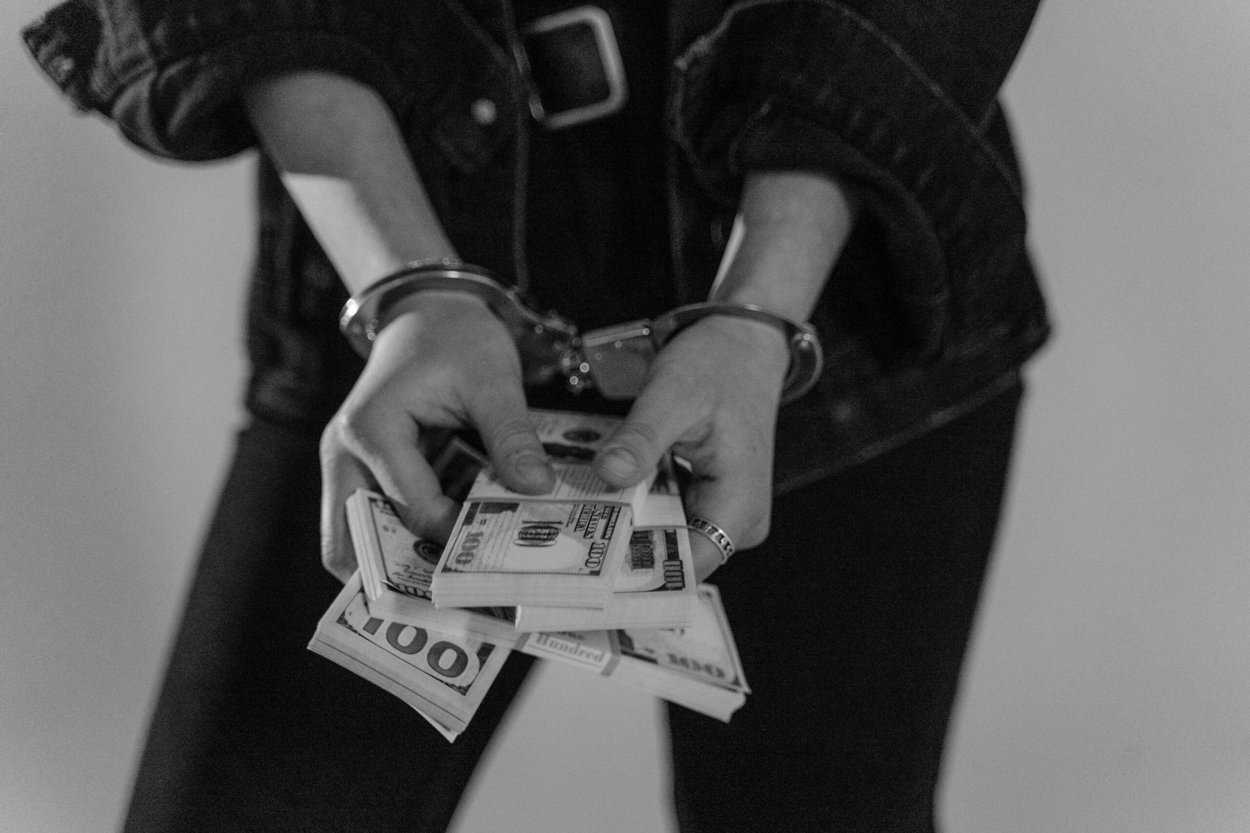 Handcuffed person holding a stack of $100 bills. Corruption, bribery.